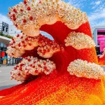 Tall red and orange LEGO wave topped with white daisy-like flowers against a blue sky