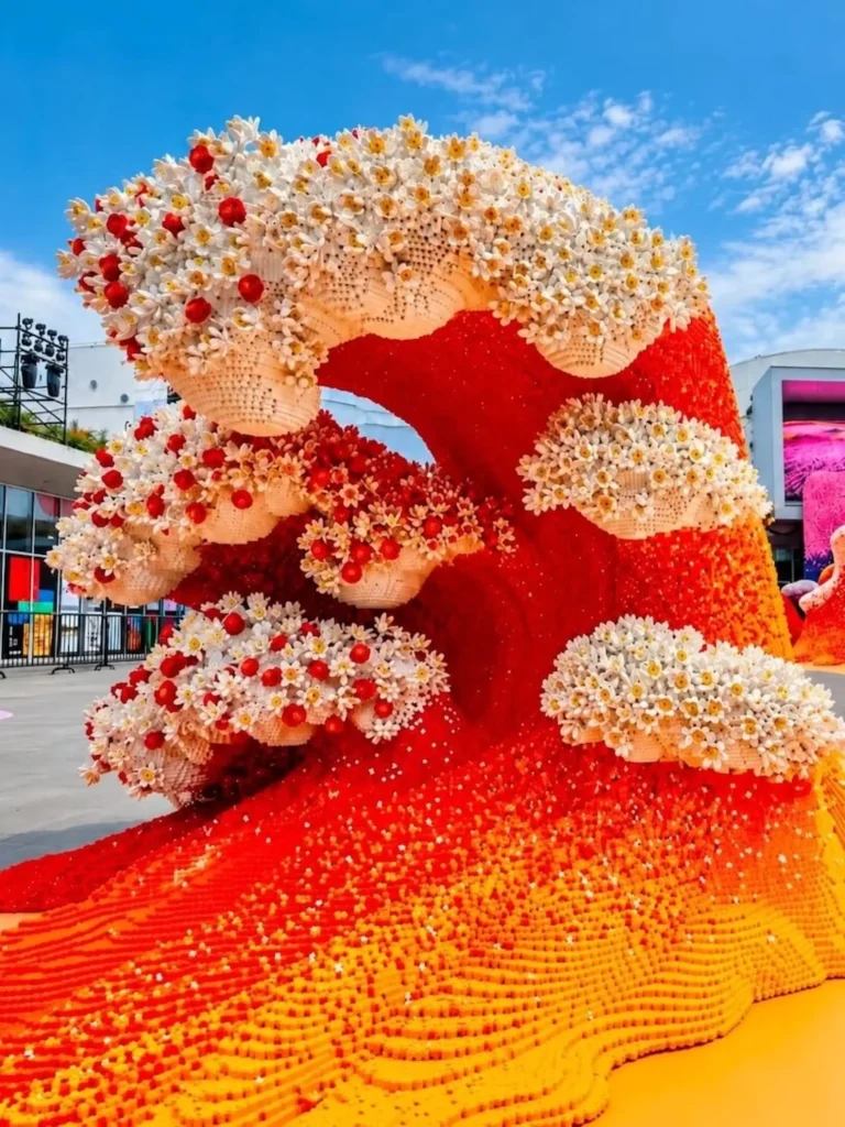 Tall red and orange LEGO wave topped with white daisy-like flowers against a blue sky