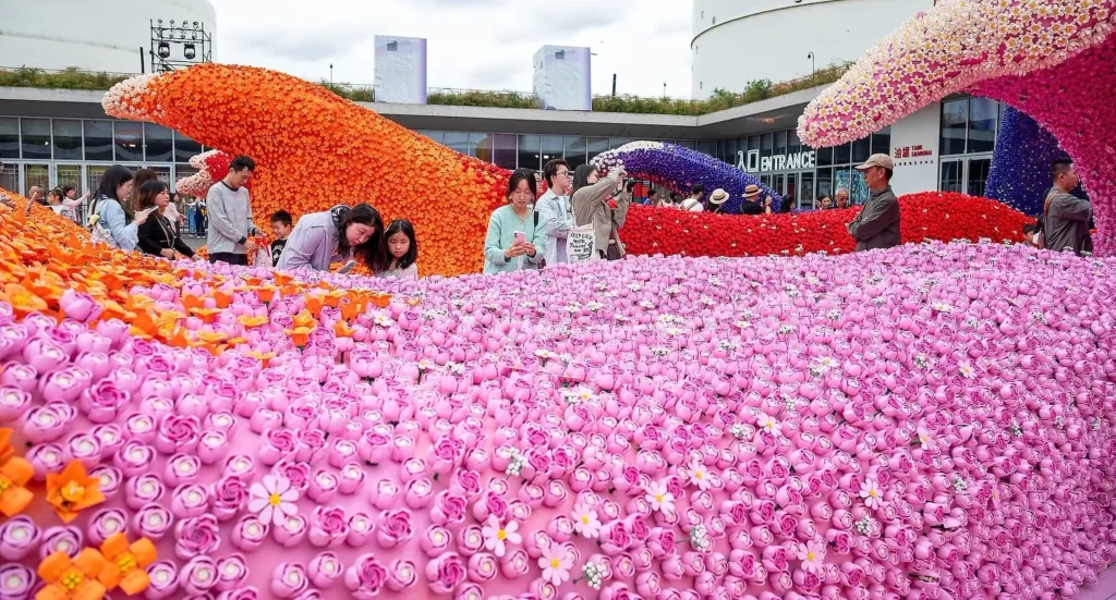 Families and visitors examining a wide field of pink LEGO roses with larger orange and purple waves in the background