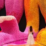 Woman in a polka-dot dress standing before towering pink and orange LEGO flower walls inside the exhibition space