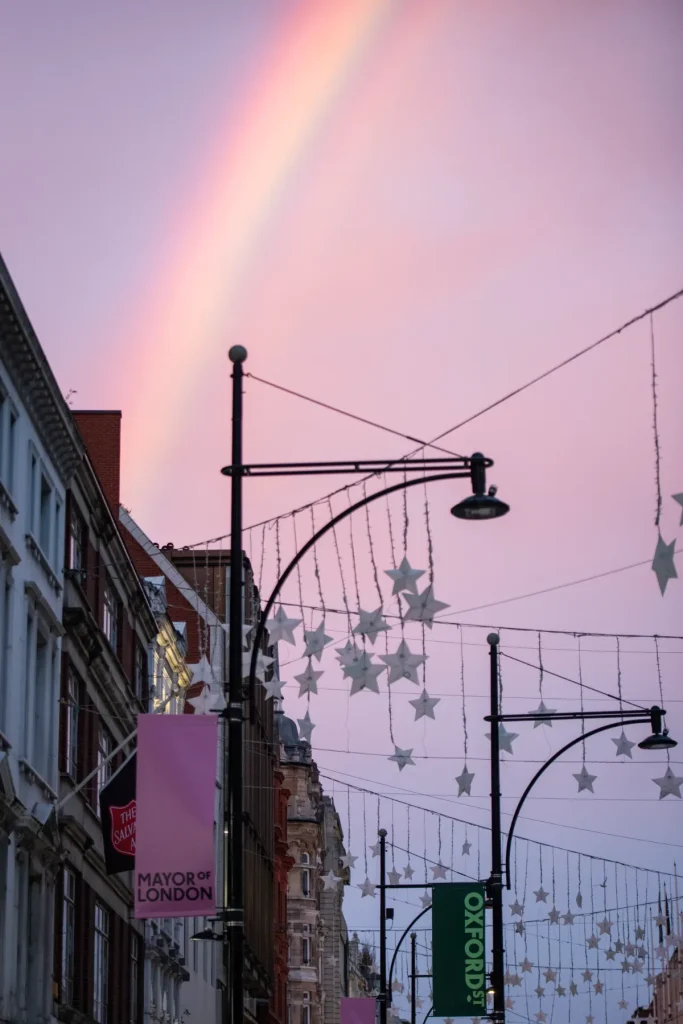 Rainbow over Oxford Street in central London, with festive star decorations, historic buildings, and street banners ahead of the pedestrianization project