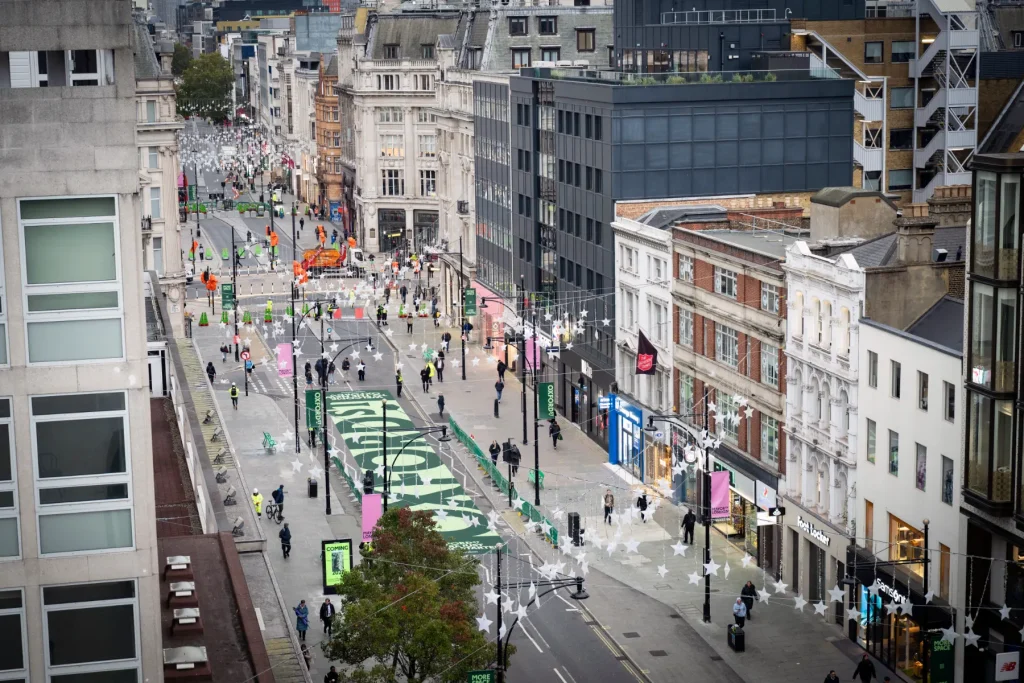Aerial view of Oxford Street in London during pedestrianization preparations, showing temporary road closures, green street graphics, pedestrians, and surrounding commercial buildings