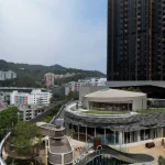 Exterior view of Sky House with outdoor playground, slides and net structures set against residential towers and green hills