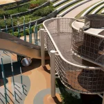 Close view of outdoor playground equipment including a curved metal slide, net tower and vertical poles beside terraced planting
