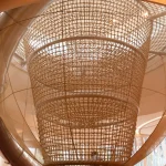 Looking upward into a large cylindrical rope-climbing net suspended beneath a skylight
