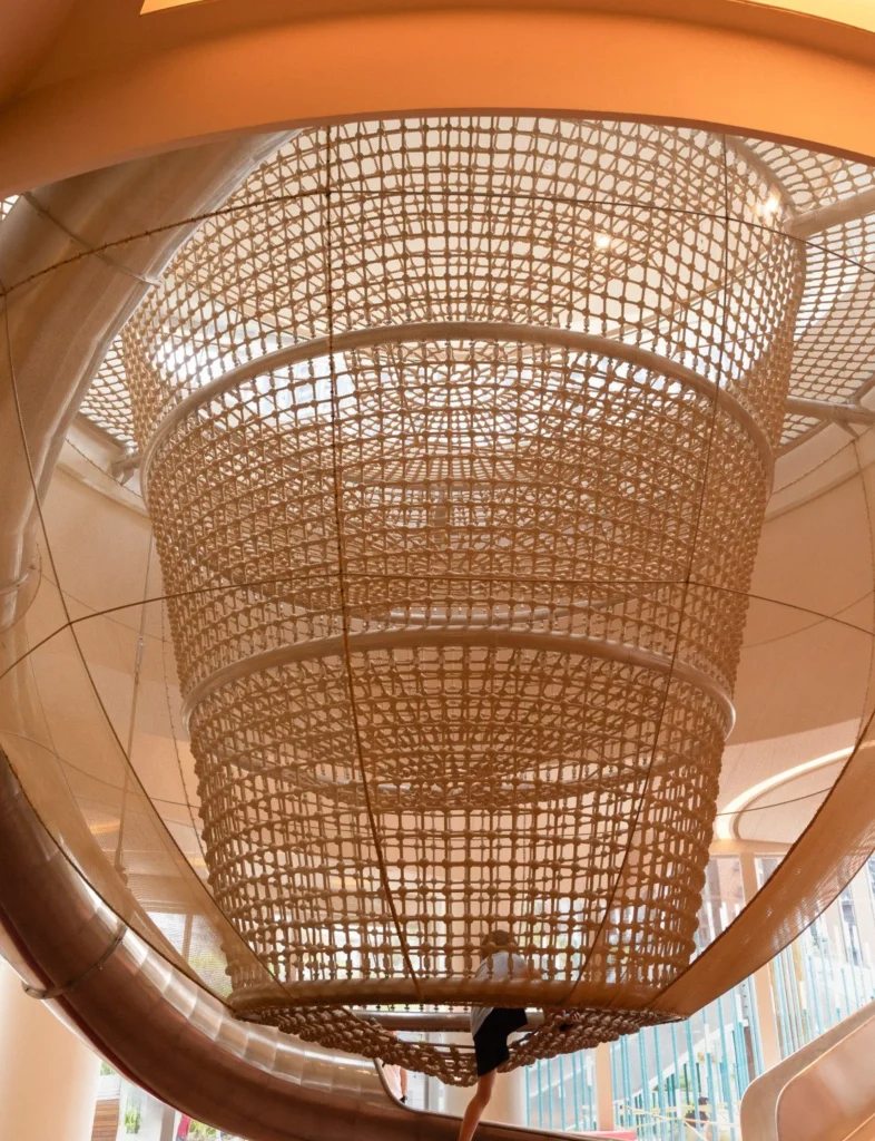 Looking upward into a large cylindrical rope-climbing net suspended beneath a skylight