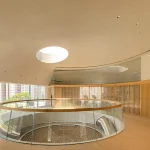 Upper-level circular gallery with glass balustrade overlooking the climbing net and a central skylight