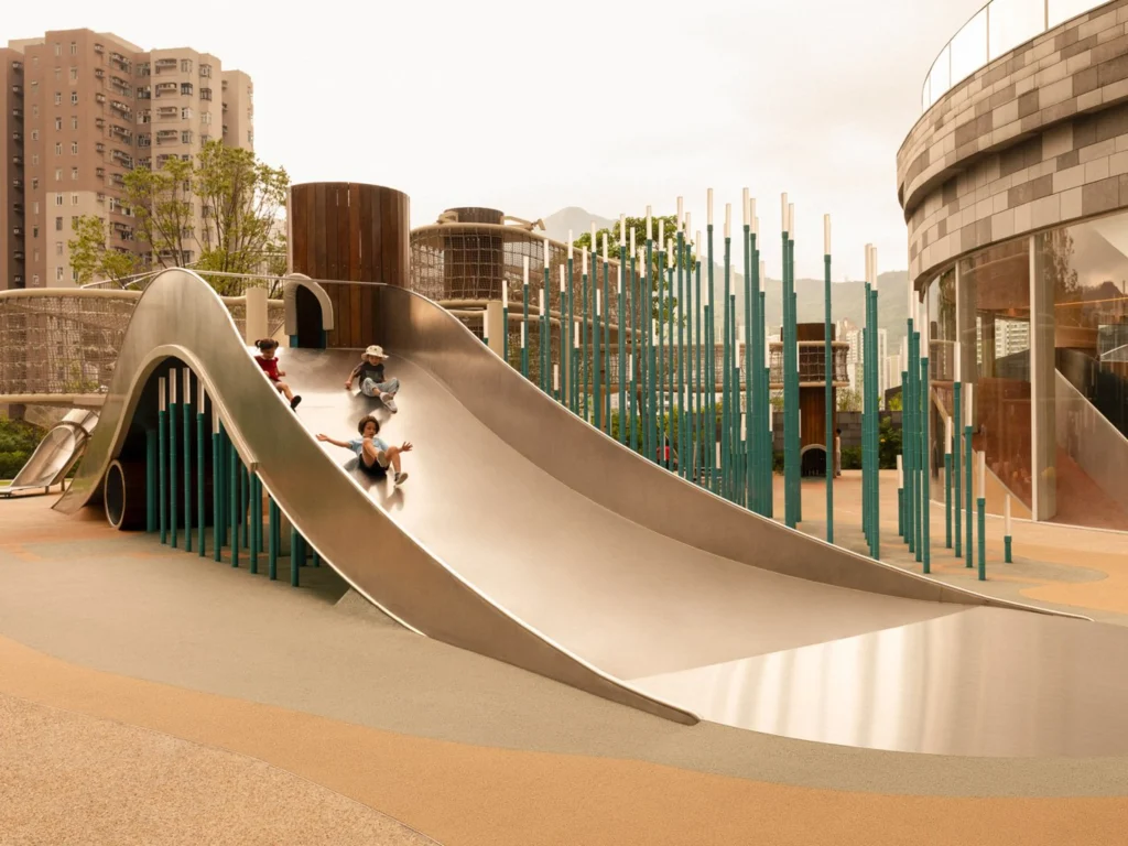 Children sliding down a large curved stainless-steel slide in the outdoor playground