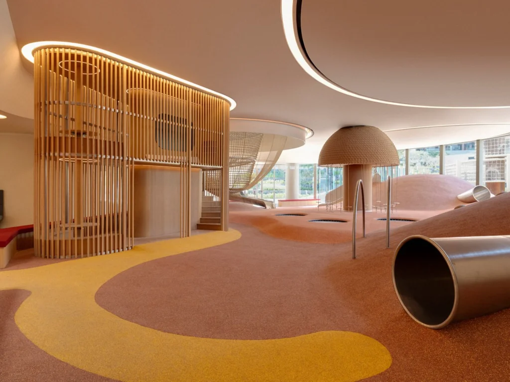Wide view of the indoor play area with wooden slat structures, soft coloured flooring and climbing elements