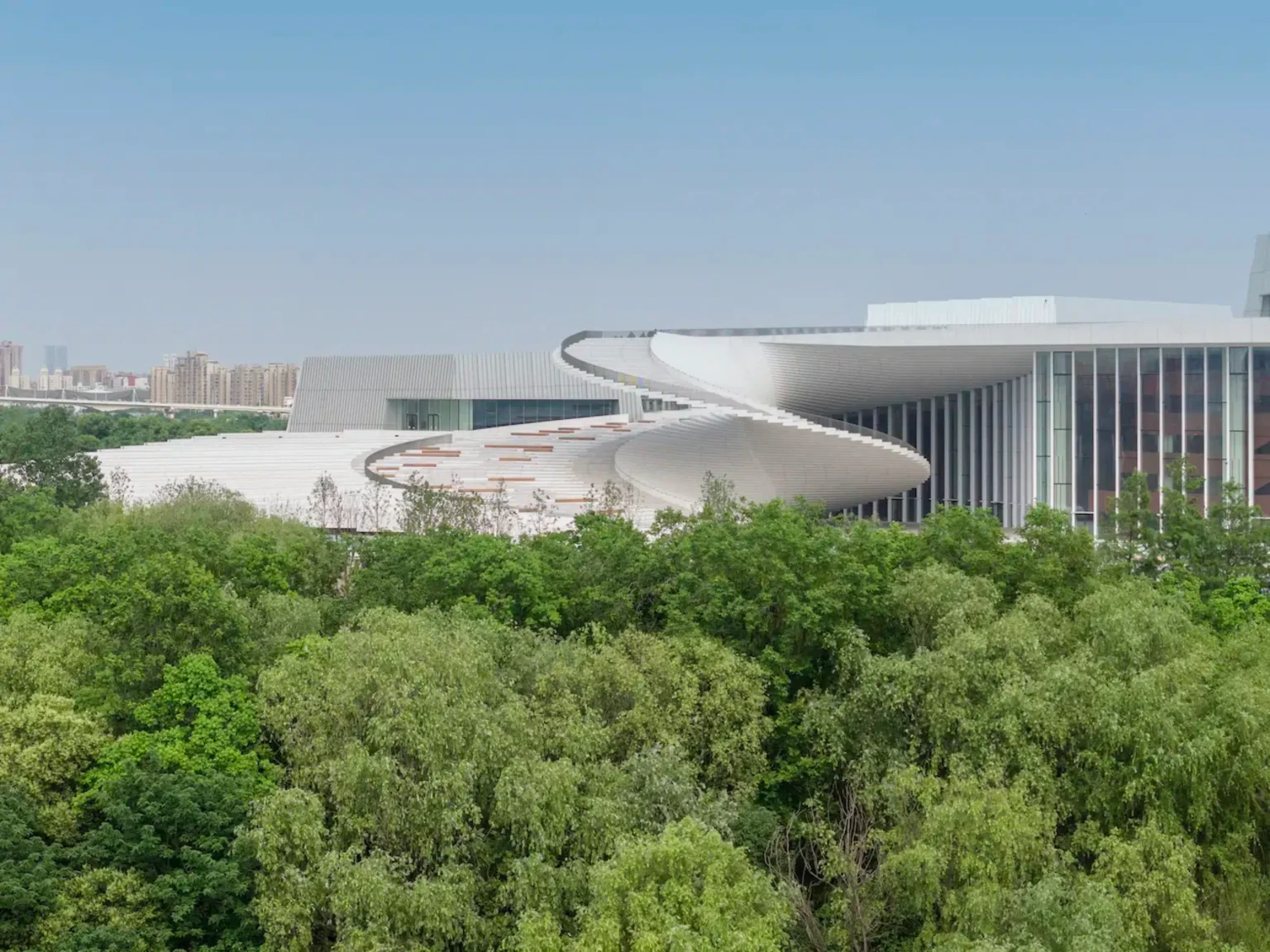 Exterior view of the Shanghai Grand Opera House’s white helical roof rising above dense green trees