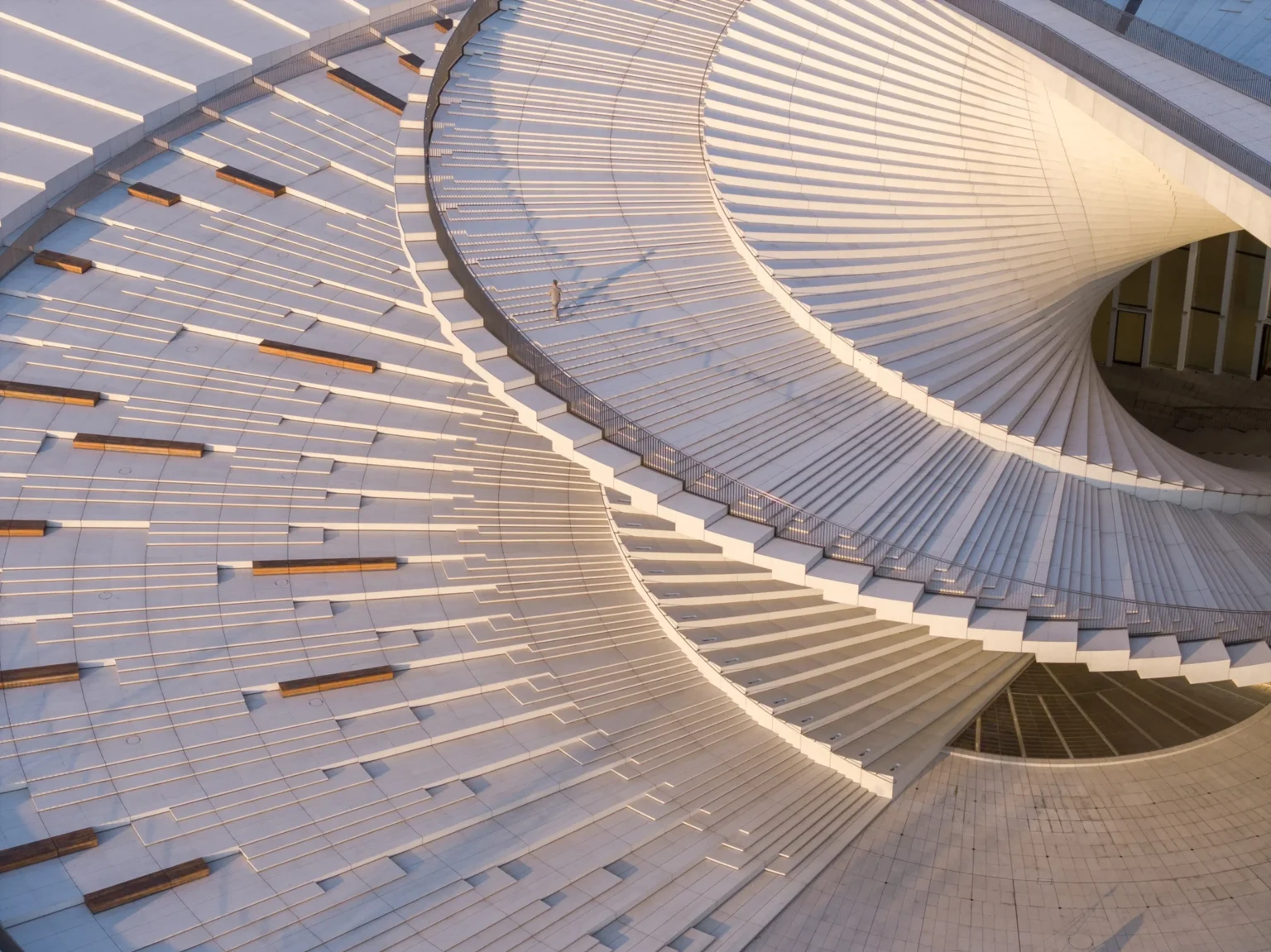Aerial close-up of the spiraling white roof terrace with wooden benches and a single person walking