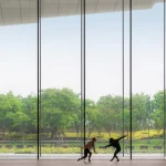 Two dancers silhouetted against floor-to-ceiling glass looking out to trees and open landscape