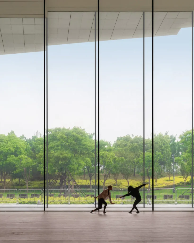 Two dancers silhouetted against floor-to-ceiling glass looking out to trees and open landscape