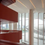 Interior view of red curving walls and high windows framing the white helical roof outside