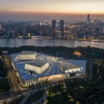 Dusk aerial of the fully lit opera house complex beside the Huangpu River and Shanghai skyline