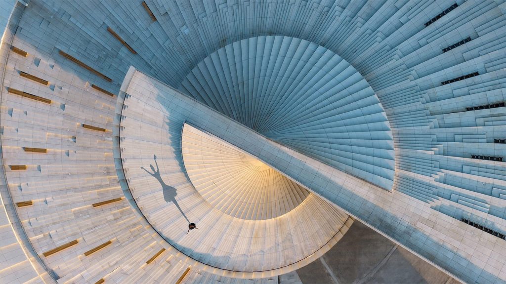 Overhead view of the spiral roof with a dancer’s long shadow stretching across the white stepped surface
