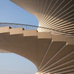 Close-up of the underside of the curving roof and stepped edge with metal railing against the sky