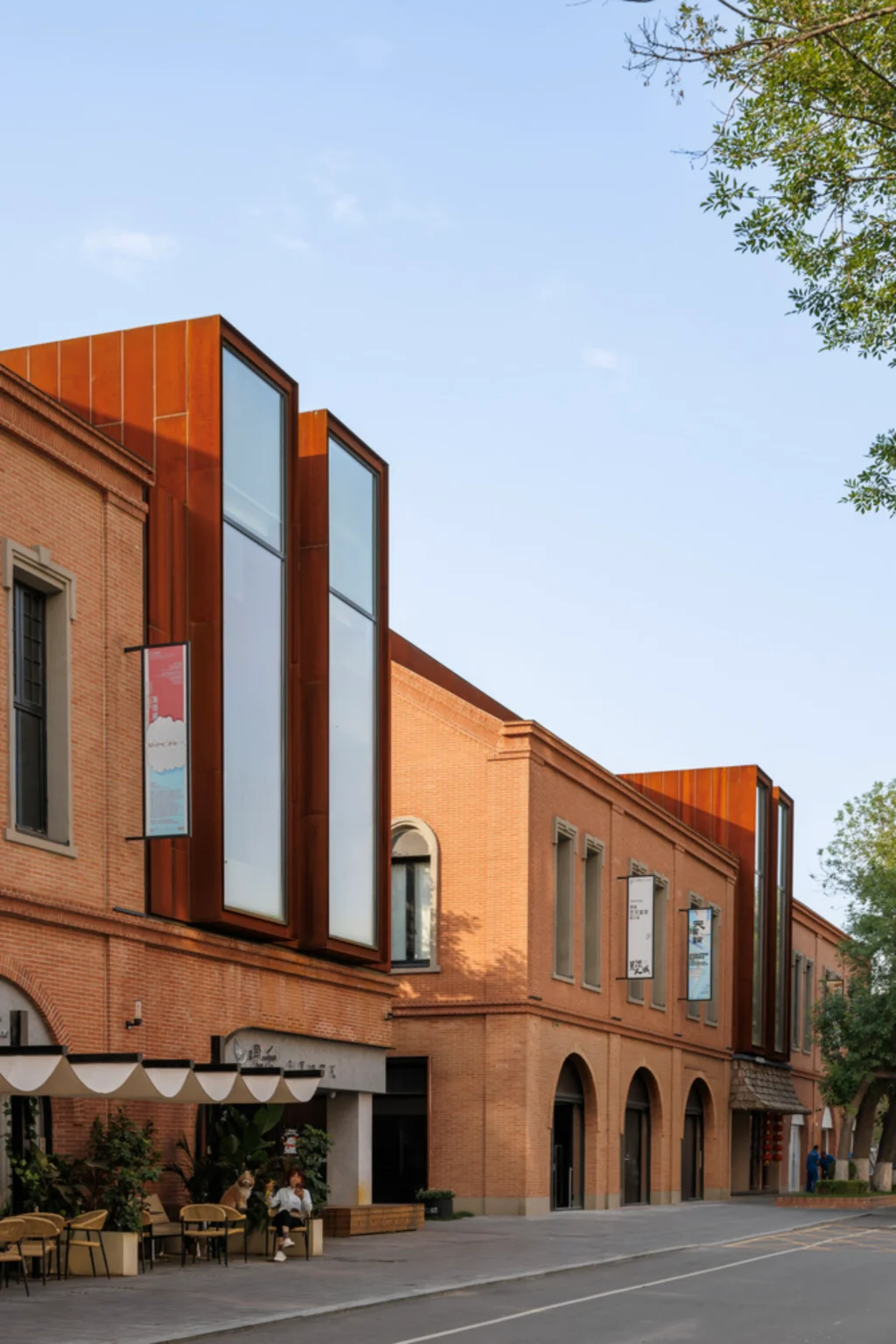Row of brick buildings with tall corten steel window insertions and ground-floor cafés