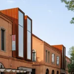 Row of brick buildings with tall corten steel window insertions and ground-floor cafés