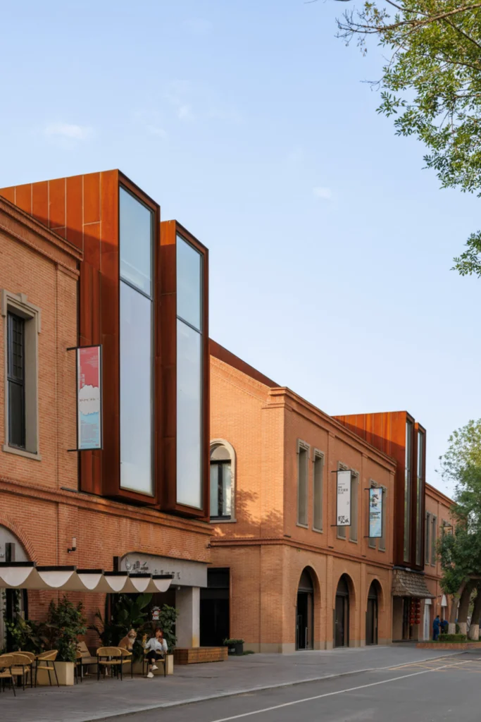 Row of brick buildings with tall corten steel window insertions and ground-floor cafés