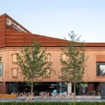 Mixed brick and corten steel building with outdoor seating and café terrace at ground level