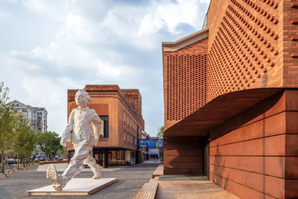 Large white figurative sculpture of a walking child set against red brick buildings with patterned façades