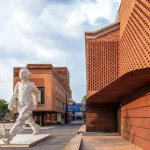 Large white figurative sculpture of a walking child set against red brick buildings with patterned façades