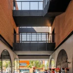 Narrow passageway between brick buildings with black steel bridges overhead and visitors looking upward