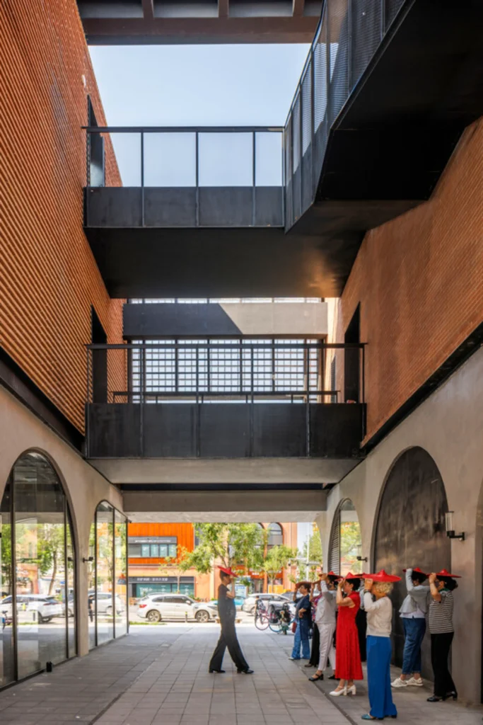 Narrow passageway between brick buildings with black steel bridges overhead and visitors looking upward