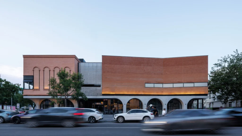 Street-facing brick and concrete building with arched ground-floor openings and warm evening lighting