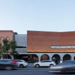Street-facing brick and concrete building with arched ground-floor openings and warm evening lighting
