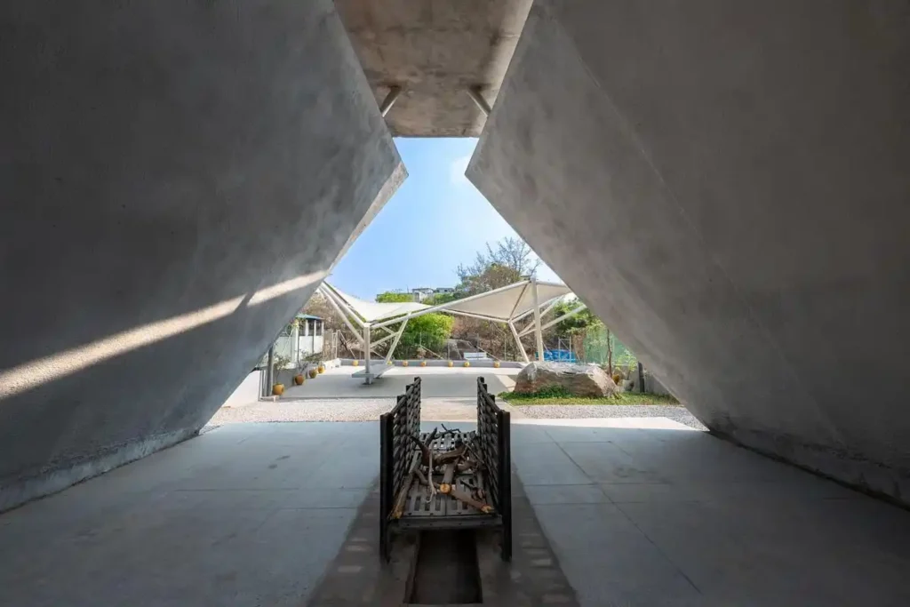 Interior view looking out from beneath a concrete pyre toward the open sky and tensile waiting structures beyond