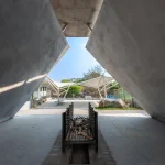 Interior view looking out from beneath a concrete pyre toward the open sky and tensile waiting structures beyond