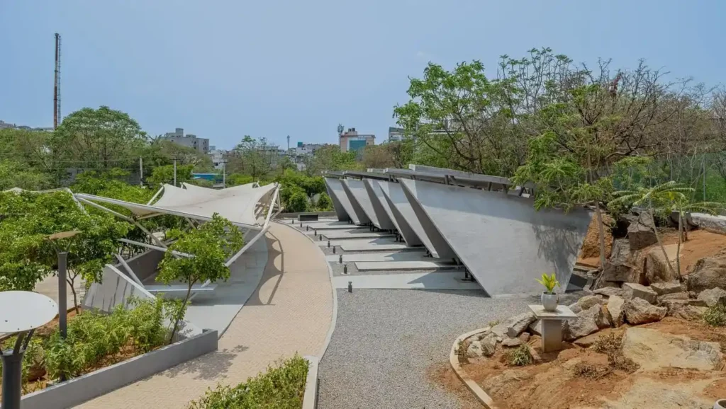 Series of angled concrete pyre structures and tensile fabric waiting canopies arranged along a curved pathway in a landscaped setting