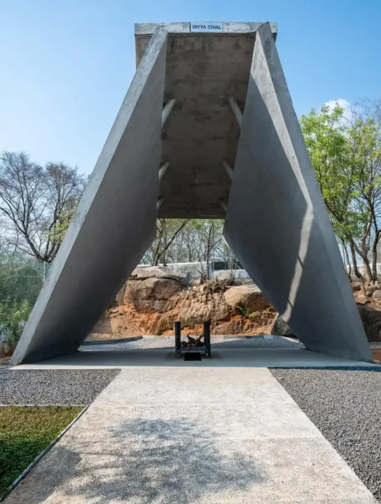 Concrete pyre structure formed by two large angled planes rising over a central fire grate, labelled Divya Sthal