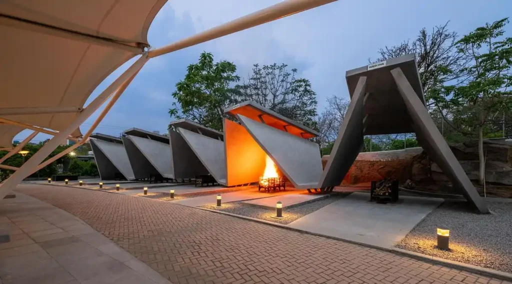 Night view of the Vaikuntha Mahaprasthanam Crematorium with one structure glowing from an active fire while pathway lights illuminate the ground
