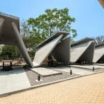 Row of angular concrete pyre structures with open sides and waiting benches, labelled Moksh Sthal under a clear sky