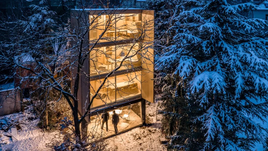 Night view of the glowing three-storey Wardrobe House with open shutters, people under the raised base, and snow-covered trees