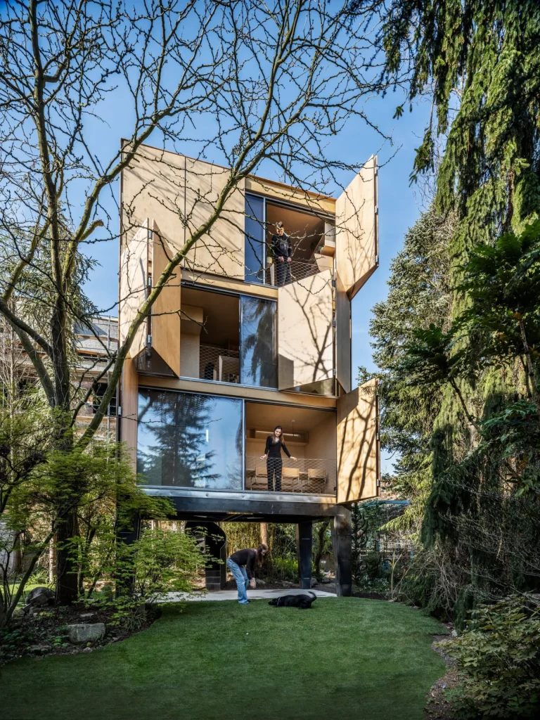 House with large shutters swung open on multiple levels, people visible on the floors and in the garden with a dog