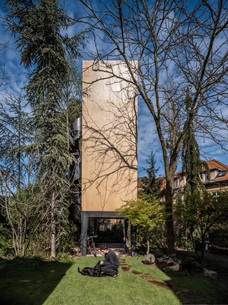 Side view of the narrow plywood tower on steel legs, with a person and dog on the lawn