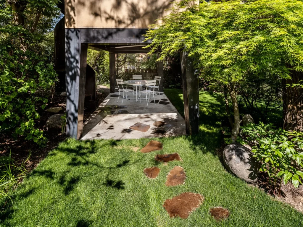 Covered outdoor seating area beneath the raised house with table, chairs and stepping stones