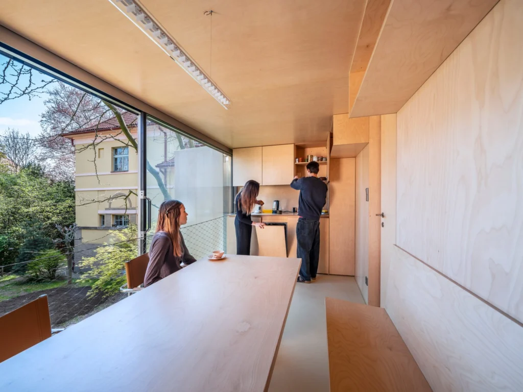 Interior of the plywood kitchen and dining level with large window and three people preparing food