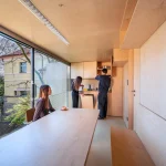 Interior of the plywood kitchen and dining level with large window and three people preparing food