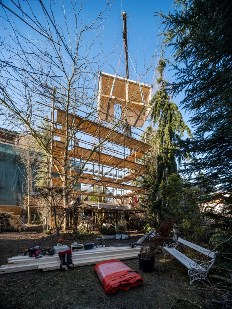 Prefabricated timber module being lifted by crane onto the scaffolded structure during construction