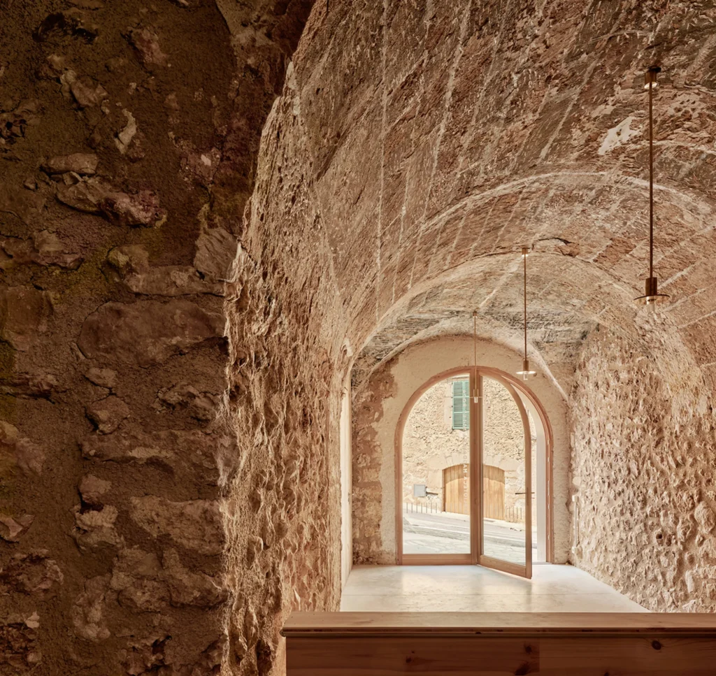 Vaulted stone interior with rough textured walls and an open arched doorway looking onto a sunlit street