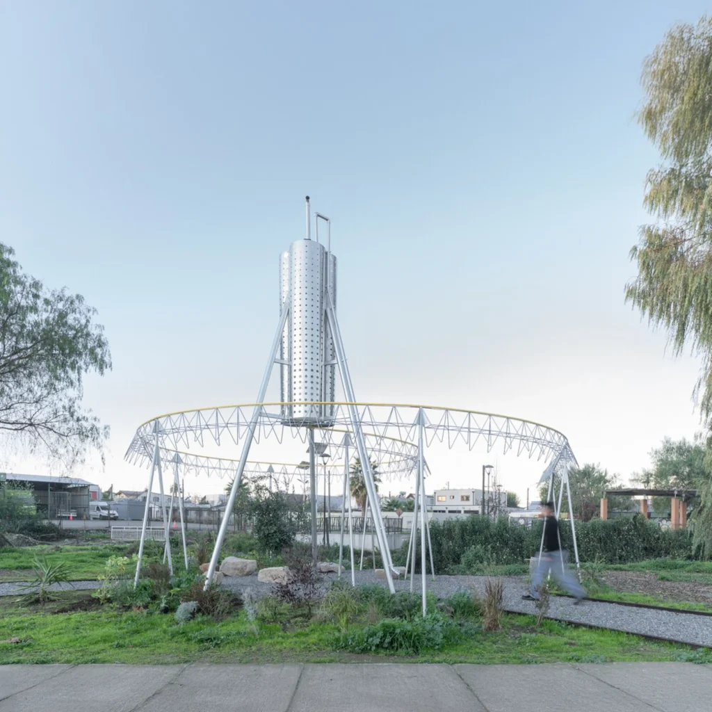 Circular metal framework supporting a perforated cylindrical tower in a small urban park