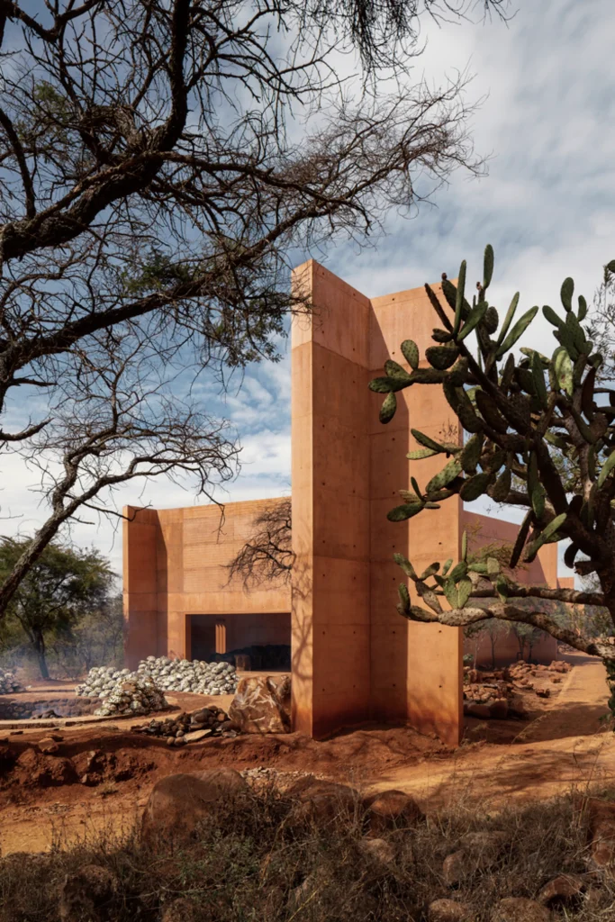 Earth-toned concrete chapel structure standing among dry trees and cacti in an arid landscape
