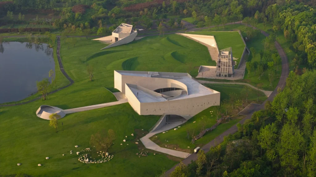 Golden-hour aerial view of the entire Zi Museum complex, showing the main courtyard building, amphitheatre-like form, meditation tower and grass-covered workshop