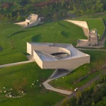 Golden-hour aerial view of the entire Zi Museum complex, showing the main courtyard building, amphitheatre-like form, meditation tower and grass-covered workshop