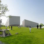 People relaxing, walking and picnicking on the grassy slopes in front of the pale concrete museum buildings under a clear blue sky